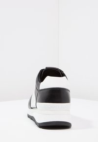 Černobílé kožené tenisky s křivkovým designem, výrazným podpatkem, texturovanými akcenty a logem na zadní straně.