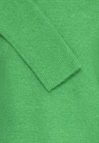 Žalias megztinis su minkšta tekstūra, raštuotais rankogaliais ir šiek tiek laisvu siluetu, kuriame tolygiai paskirstyta spalva per visą audinį.