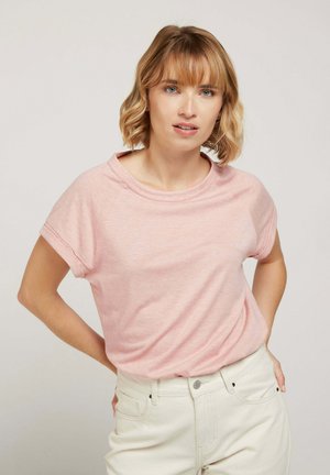 Haut rose à manches courtes avec un col rond et des manches repliées. Tissu doux et léger, associé à un pantalon blanc taille haute.
