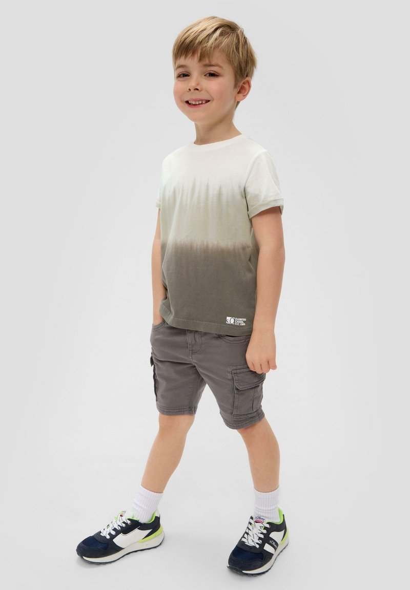 Katoenen T-shirt met een gradiënt van lichtbeige naar donkergrijs, gecombineerd met grijze cargoshorts. Zwart-witte sneakers met groene accenten.