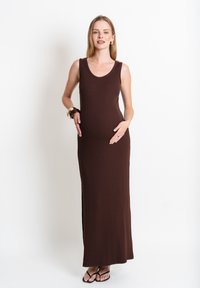 Brązowa, bezrękawnikowa sukienka maxi wykonana z miękkiego materiału, z okrągłym dekoltem i bocznymi rozcięciami, noszona przez modelkę z brzuszkiem ciążowym.