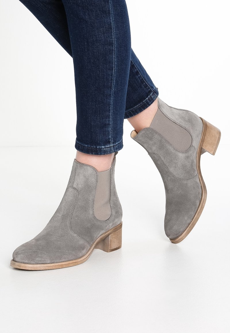 Botines de ante gris con paneles laterales elásticos y tacón bloque de madera, que presentan una textura suave y un diseño de punta redondeada.