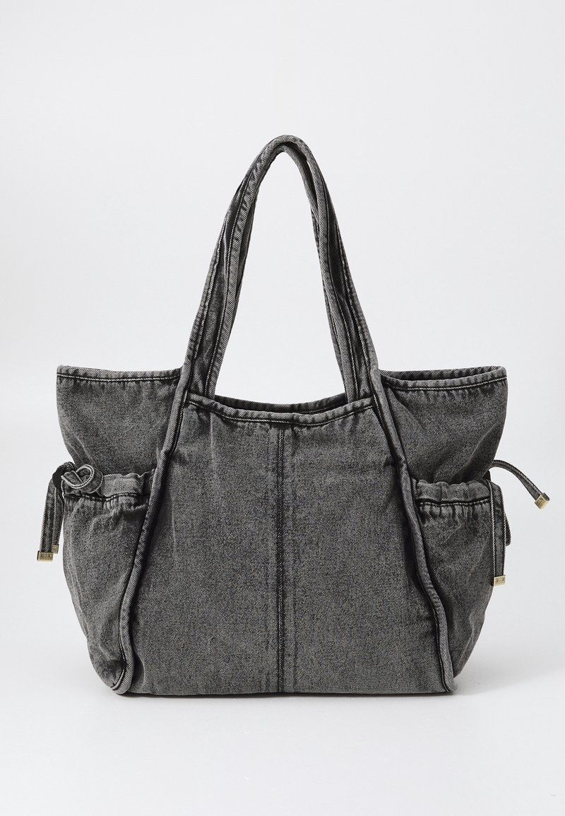 Sac fourre-tout en denim gris avec doubles bretelles, compartiment principal spacieux et deux poches extérieures à cordon de serrage de chaque côté.