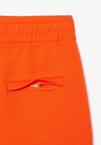 Ljusa orange joggers med elastisk midja och en liten dragkedjeficka. Tillverkad av mjukt material med en jämn och slät yta.