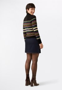 Gestreifter Strickpullover mit schwarzen, grünen, roten und gelben Linien. Kombiniert mit einem dunklen Jeansrock und glanzvollen braunen Stiefeletten.