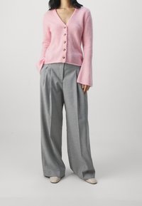 Rosa fluffig cardigan med V-udskärning och träknappar, matchad med grå vida byxor. Skorna är ljusa, spetsiga.