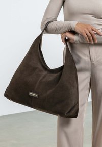Bruine suede hobo tas met een slouchy vorm, contrasterende stiksels, logo label en accessoires in goudkleurige hardware. Soepele, zachte textuur.