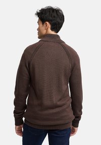 Brun strikket sweater med høj krave, ribstrikkede ærmegab og subtilt tekstureret stof. Har raglanærmer og en afslappet pasform.