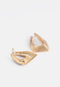 Boucles d'oreilles dorées avec des formes abstraites ; l'une présente une surface lisse, l'autre a un design texturé et strié. Support transparent inclus.