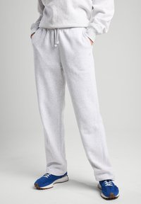 Pantaloni jogger grigi in pile con vita regolabile, tasche laterali e una vestibilità comoda, abbinati a scarpe da ginnastica blu.