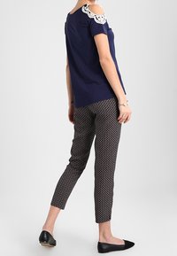 Top de hombros al descubierto en azul marino con detalles de encaje blanco, combinado con pantalones negros con un patrón. La modelo lleva zapatos planos negros. Un atuendo simple y casual.