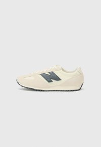 Light cream suede sneaker with a dark blue "N" logo. Features a textured upper, white laces, and a black rubber sole.