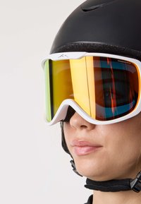 Skibril met een wit montuur en een geel-oranje gespiegelde lens; opvallende kenmerken zijn de gebogen vorm en het brede zicht voor goede zichtbaarheid. Zwarte helm gedragen.