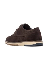 Zapato de ante marrón con puntera redondeada, suela resistente con acentos en beige y azul oscuro, y diseño con cordones. El talón trasero presenta una pequeña asa.