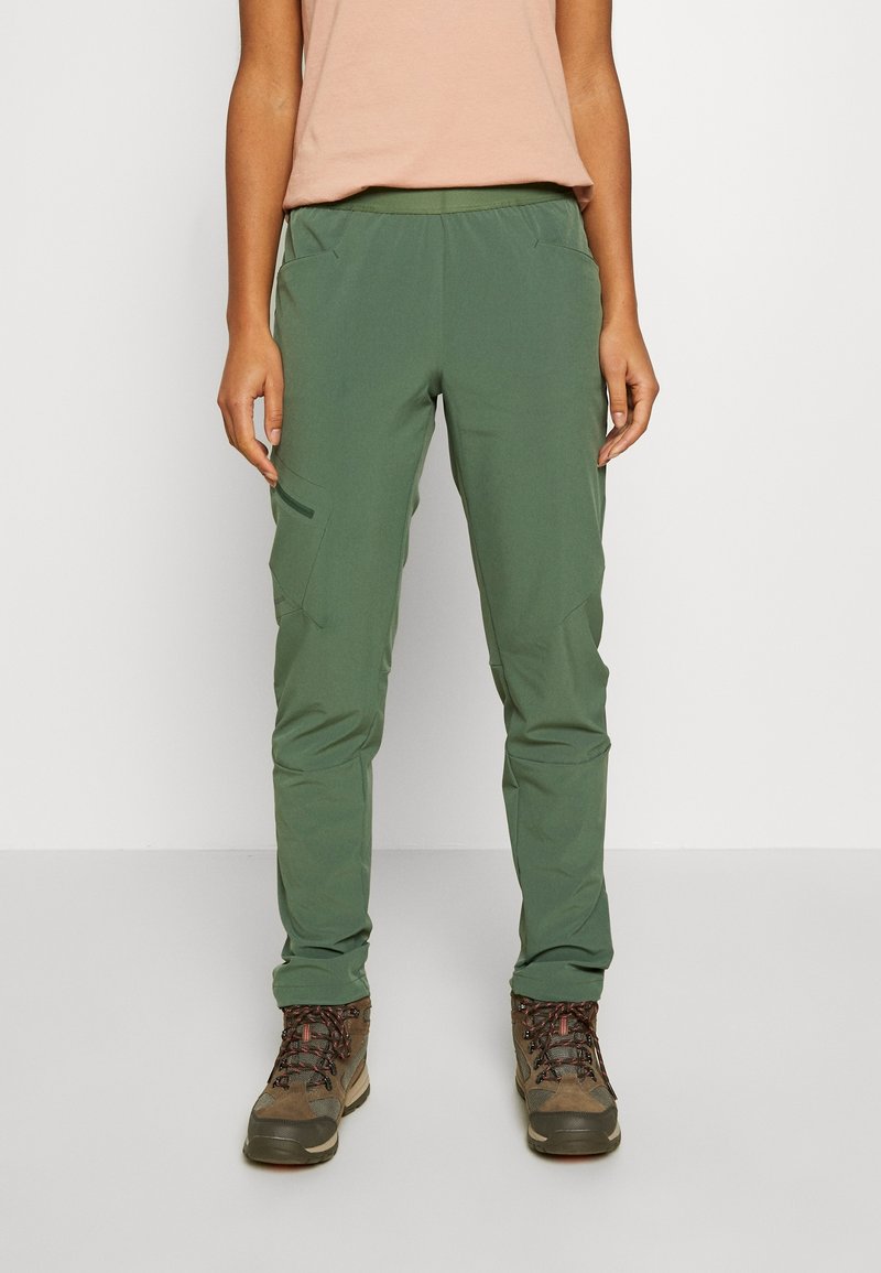 Groene wandelbroek met een taps toelopende pasvorm, elastische tailleband en zijzakken, gecombineerd met grijze en bruine wandelschoenen.