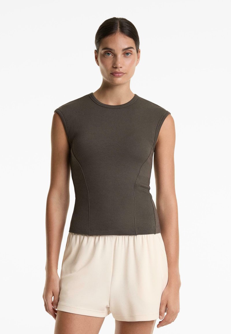 Donkergroen mouwloos topje met een geribbelde textuur en een aangesloten pasvorm, gecombineerd met lichtbeige shorts met een trekkoord.