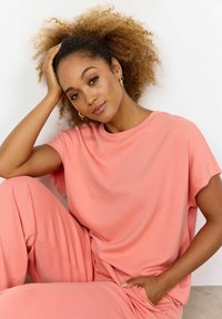 Roze loungewearset van gladde stof, bestaande uit een losvallende top met korte mouwen en bijpassende broek, met een ontspannen silhouet.