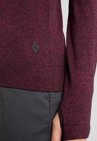 Burgundy långärmad skjorta i strukturerad tyg med logodetalj i svart; kombinerad med mörkgrå byxor med en synlig ficka.