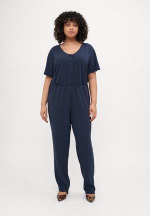 Combinaison bleu marine à manches courtes, décolleté en V, devant à boutons et taille élastique ; tissu lisse avec une coupe décontractée. Les talons ont un imprimé léopard.