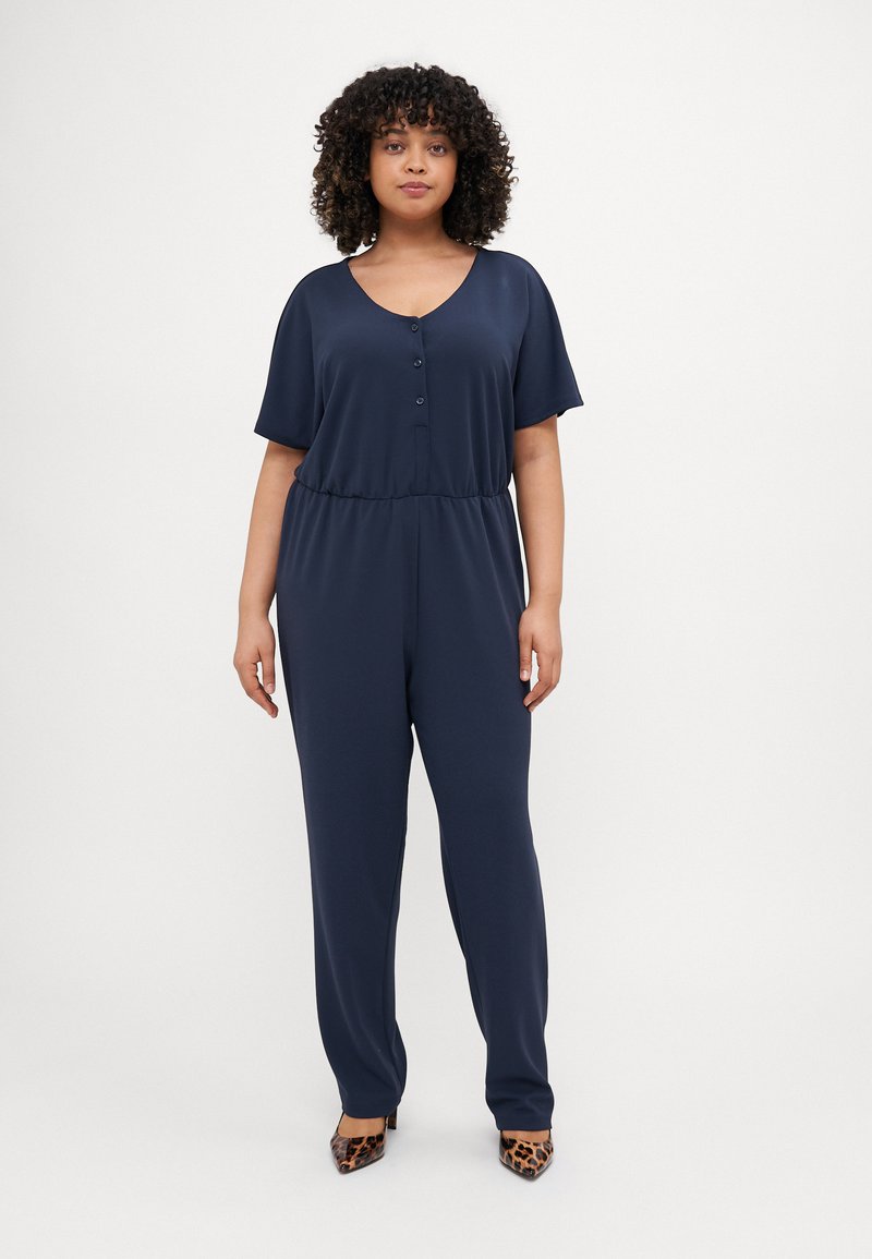 Navy blue jumpsuit with short sleeves, V-neck, button front, and elastic waistband; smooth fabric with a relaxed fit. Heels have a leopard print.