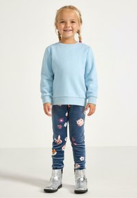 Felpa azzurro chiaro con maniche lunghe, abbinata a leggings blu con motivi colorati di animali e fiori, e stivaletti argento alla caviglia.