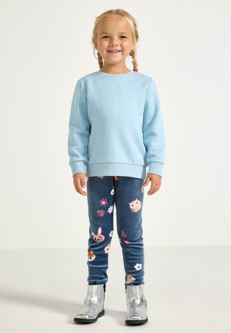 Felpa azzurro chiaro con maniche lunghe, abbinata a leggings blu con motivi colorati di animali e fiori, e stivaletti argento alla caviglia.
