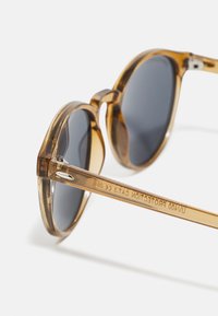 Korytnačkové slnečné okuliare s okrúhlymi rámy, sivými sklami a lesklým povrchom. Obsahujú jasné detaily na ramene.