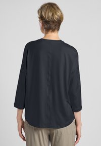 Dunkelgrauer, leichter Pullover mit 3/4-Ärmeln, abgerundetem Saum und glatter Textur. Die Nahtdetails verlaufen vertikal über den Rücken.