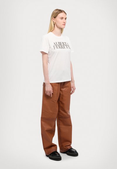Weißes Baumwoll-T-Shirt mit grauem Aufdruck "ALBERT FERRETTI". Kombiniert mit braunen, strukturierten, weiten Hosen und schwarzen Plateau-Schuhen.