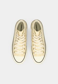 Αθλητικά παπούτσια ύψους, φτιαγμένα από ένα υλικό με υφή σε κρεμ χρώμα. Διαθέτουν μπεζ κορδόνια, μαύρη σόλα από καουτσούκ και λευκή μύτη με μαύρη περι edging.