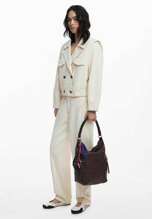 Veste cropped crème avec poches avant et couture contrastante, assortie à un pantalon large et un sac à main slouchy marron foncé.