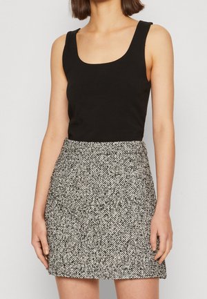 Femme portant un haut noir sans manches à encolure carrée et une mini-jupe taille haute en tweed noir et blanc, debout les bras détendus.