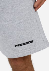 Calções de algodão cinza com uma textura suave, um corte relaxado e o logo bordado "PEGADOR" em preto no lado inferior esquerdo.
