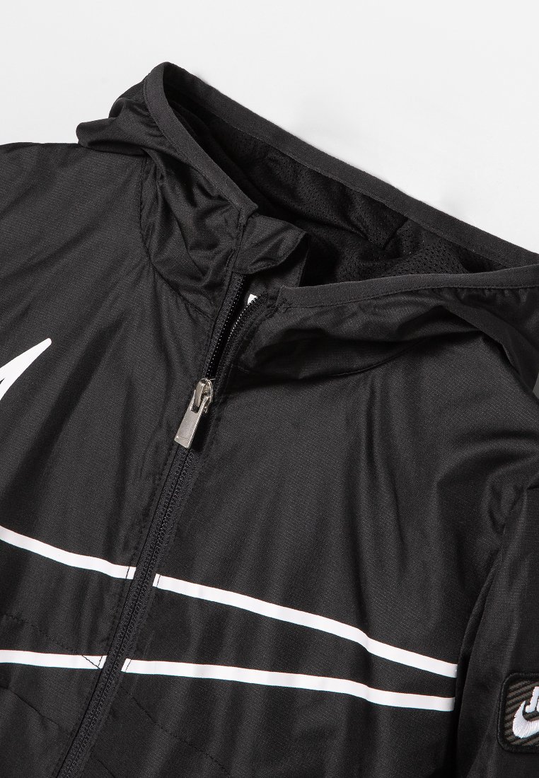 Veste de sport noire avec fermeture éclair devant, capuche et accents à rayures blanches. Fabriquée en tissu léger avec une texture lisse.