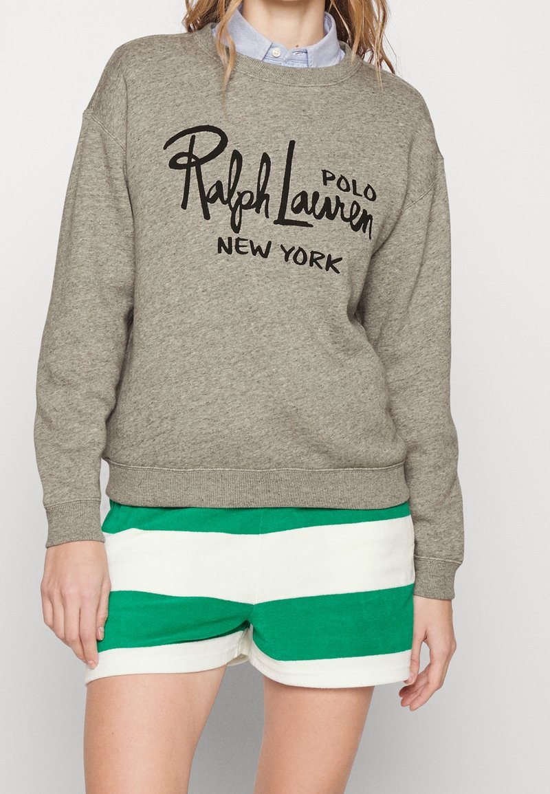 Personne portant un sweat-shirt gris Ralph Lauren à col rond, par-dessus une chemise bleue à col, et un short rayé horizontal vert et blanc.