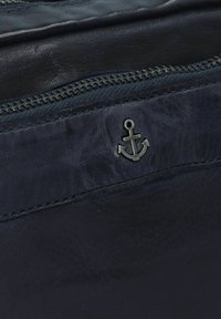 Borsa in pelle blu navy con finitura texturizzata, dotata di un emblema ad ancora argentato e di una chiusura con zip lungo il bordo superiore.