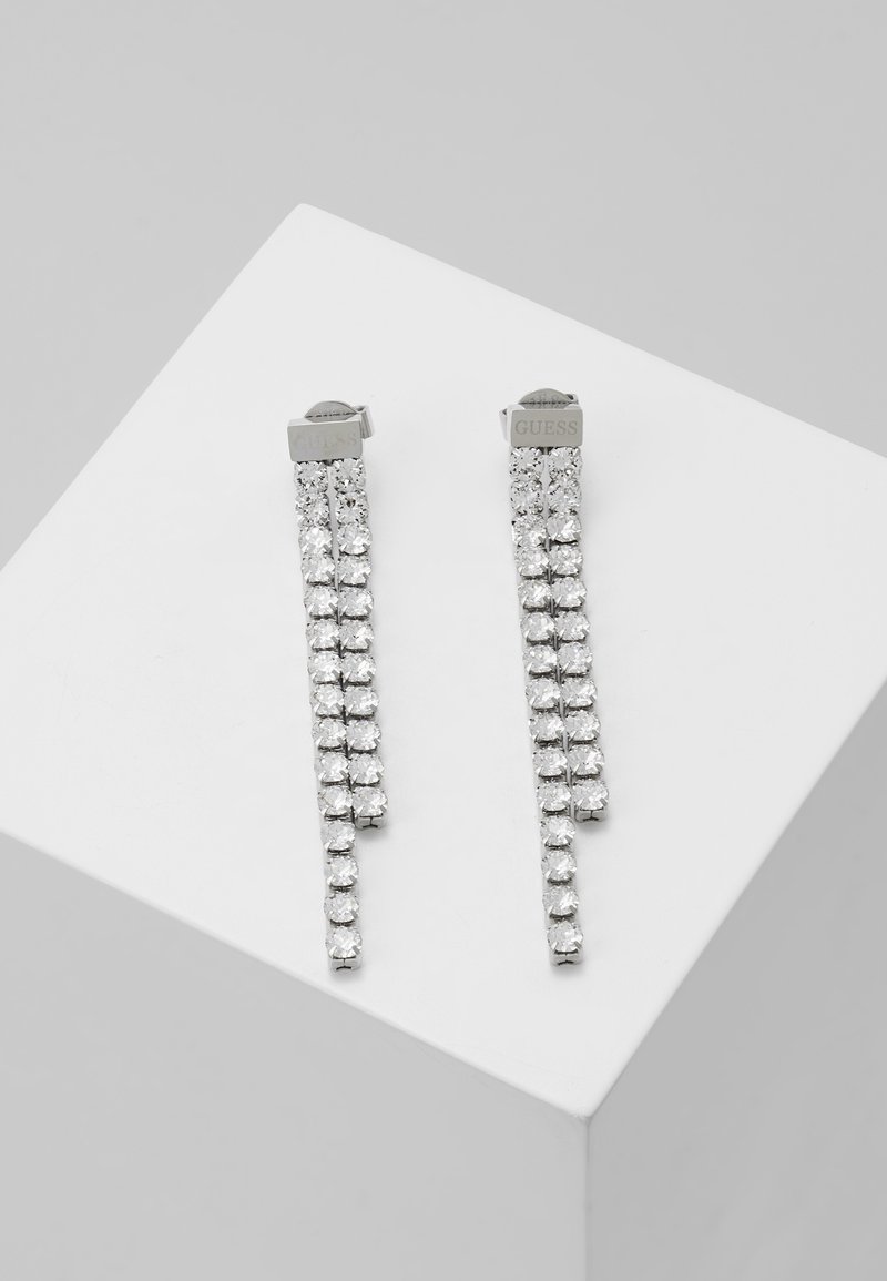 Boucles d'oreilles pendantes Guess argentées avec deux rangées de cristaux ronds transparents suspendus à un dessus rectangulaire.