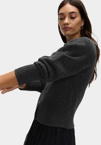 Ciemnoszary sweter z dzianiny z prążkowanymi rękawami i dopasowanym pasem, z okrągłym dekoltem i zapięciem na guziki. Miękka faktura.