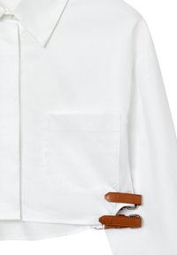 Chemise blanche courte avec un col pointu, une poche poitrine simple et des accents en cuir marron au niveau de l'ourlet. Tissu lisse et léger.