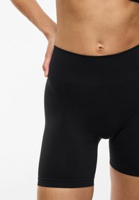 Pantalones cortos deportivos negros con una cintura alta, fabricados en un tejido suave y con un diseño hasta la rodilla. Textura blanda con detalles de costura mínimos.