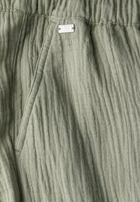 Light green, crinkled fabric with a soft texture. Features a side pocket and a label reading "Street One Studio." Elastic waistband visible.