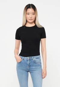 Black short-sleeve t-shirt with a fitted design, paired with light blue denim jeans. The fabric appears smooth and stretchy.