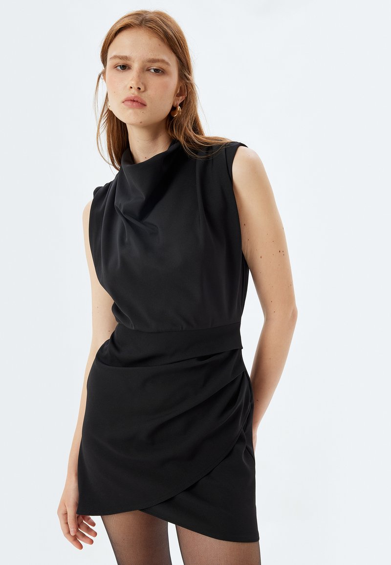 Vestido negro sin mangas con escote drapeado, cintura ajustada y falda asimétrica. Tejido suave con un brillo sutil. Diseño ligero y ajustado.