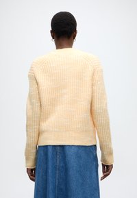 Κ ίτρινο πλεκτό πουλόβερ με υφή και σχέδιο, με ριμπ μανσέτες και τελείωμα. Συνδυασμένο με μπλε τζιν φούστα.