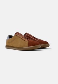 Brown and tan suede sneakers with a red toe cap, light blue heel accent, and matching brown laces on a smooth rubber sole.