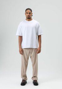 Wit T-shirt met korte mouwen, losse pasvorm; beige op maat gemaakte broek, rechte pijpen; zwarte schoenen met roze veters. Effen achtergrond, frontale weergave.