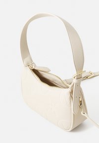 Bolso de mano de cuero crema con patrón de flores grabado, cierre de cremallera y correa ajustable. Forma compacta con textura suave.