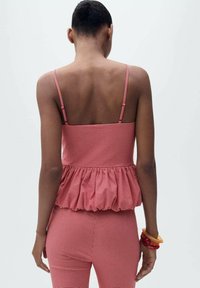 Red gingham patterned peplum top with thin straps and a textured fabric; worn with matching fitted pants, viewed from the back.