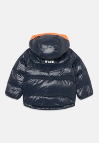 Mörkblå puffjacka med orange fodrad huva, långa ärmar och reflekterande vitt logotyp på övre ryggen, liggande platt med framsidan neråt.