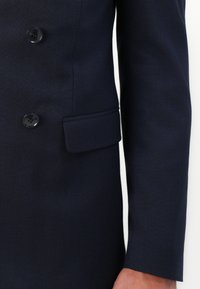 Ναυτικές διπλής όψης σακάκι με λεία ύφανση, δύο μεγάλους κομβίους, τσέπη στο αριστερό στήθος και ραμμένα μακριά μανίκια με καθαρές μανσέτες.